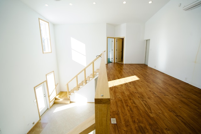 empty room with hardwood / wood-style flooring, a towering ceiling, and a wall unit AC