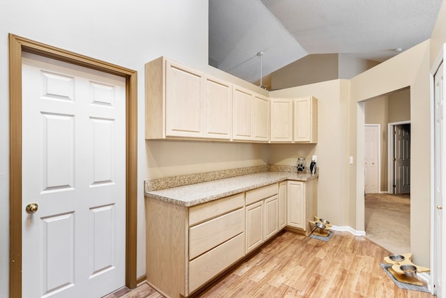 kitchen with lofted ceiling, a textured ceiling, light brown cabinets, and light wood-type flooring