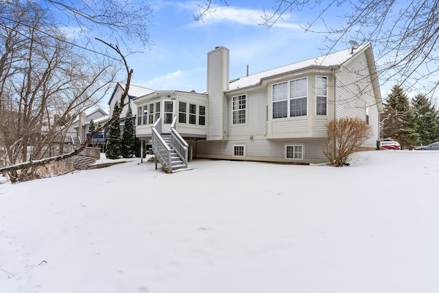 snow covered rear of property with a sunroom