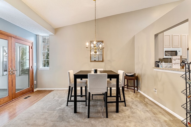 dining room featuring french doors, lofted ceiling, light hardwood / wood-style flooring, and a notable chandelier