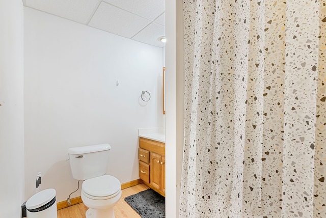 bathroom with hardwood / wood-style floors, vanity, walk in shower, toilet, and a drop ceiling