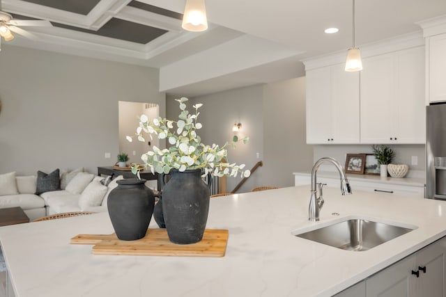 kitchen with pendant lighting, sink, white cabinetry, coffered ceiling, and light stone countertops