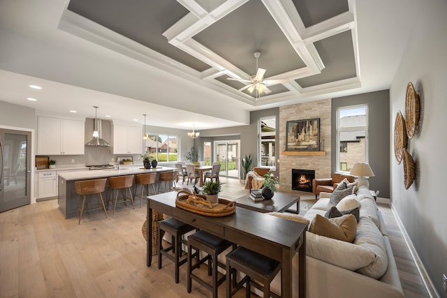 dining room with coffered ceiling, a fireplace, ceiling fan, and light hardwood / wood-style flooring