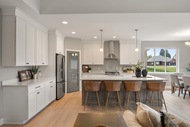 kitchen featuring stainless steel refrigerator with ice dispenser, wall chimney exhaust hood, decorative light fixtures, and white cabinets