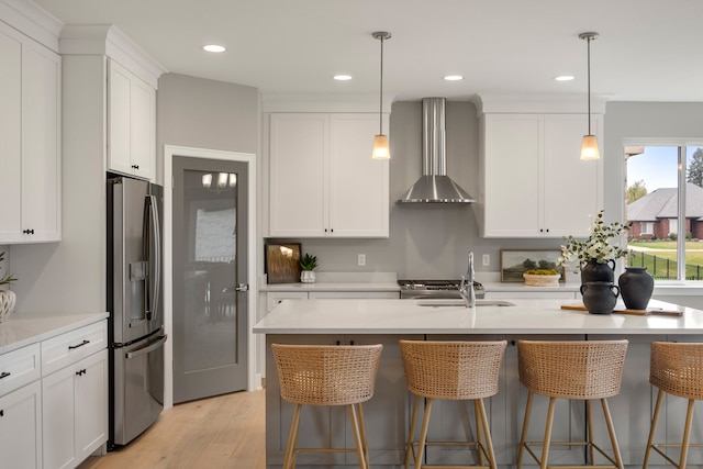 kitchen featuring stainless steel refrigerator with ice dispenser, wall chimney exhaust hood, a breakfast bar, and sink