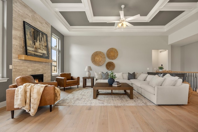 living room with coffered ceiling, a stone fireplace, and light wood-type flooring