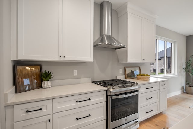 kitchen featuring white cabinetry, light hardwood / wood-style floors, gas stove, light stone countertops, and wall chimney exhaust hood