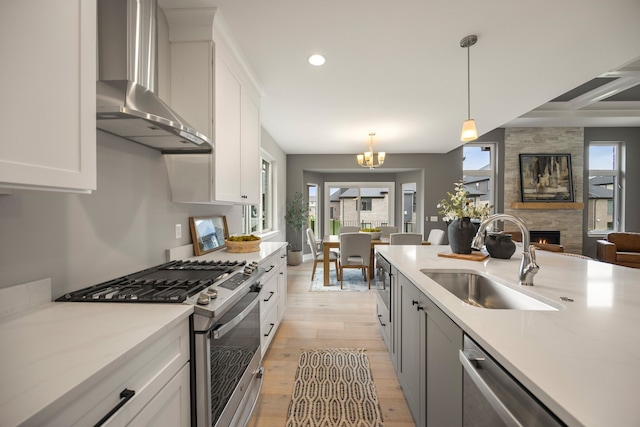 kitchen featuring appliances with stainless steel finishes, pendant lighting, white cabinetry, sink, and wall chimney range hood