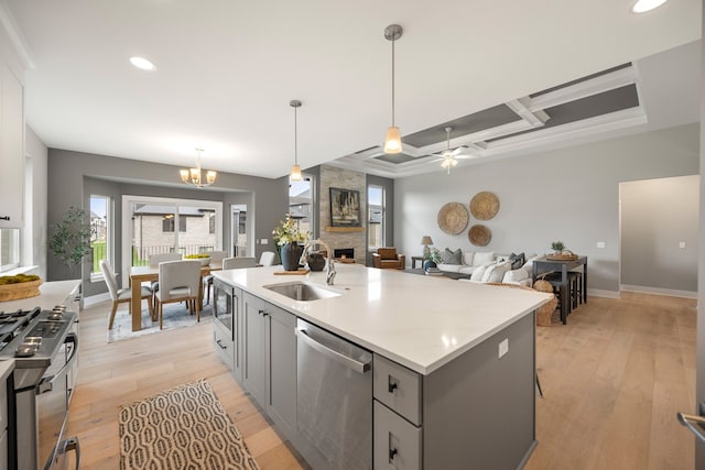 kitchen with a stone fireplace, sink, hanging light fixtures, a center island with sink, and appliances with stainless steel finishes