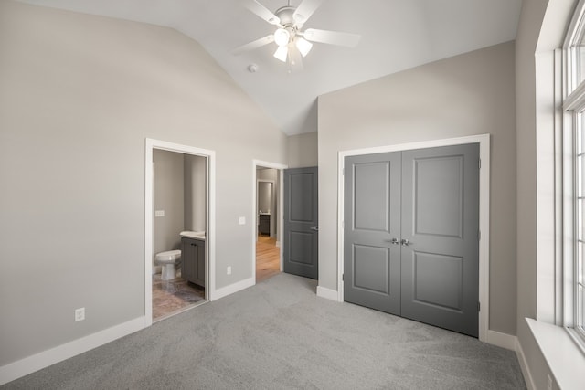 unfurnished bedroom featuring ensuite bath, ceiling fan, high vaulted ceiling, light carpet, and a closet