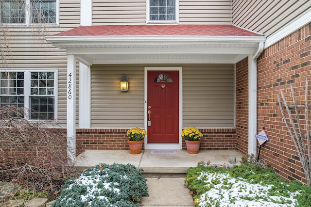 doorway to property featuring a porch, roof with shingles, and brick siding