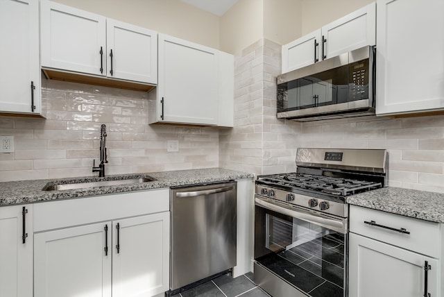 kitchen with appliances with stainless steel finishes, white cabinetry, sink, backsplash, and light stone countertops