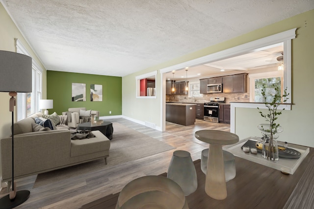 living room featuring ceiling fan, a textured ceiling, and light wood-type flooring