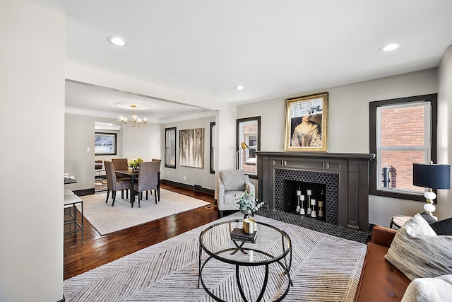 living room featuring ornamental molding, light hardwood / wood-style floors, a tile fireplace, and a notable chandelier