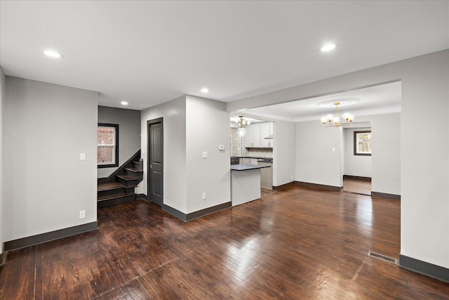 unfurnished living room with dark wood-type flooring, crown molding, and a notable chandelier