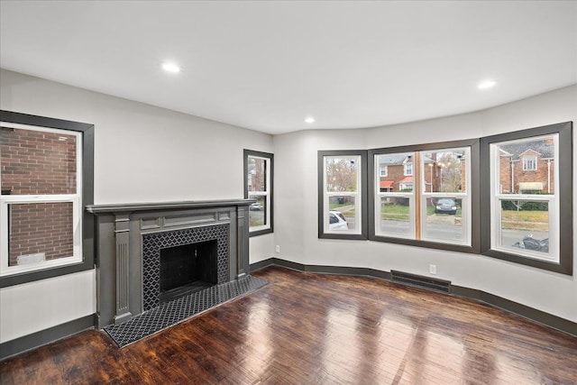 unfurnished living room featuring a tiled fireplace and dark hardwood / wood-style flooring