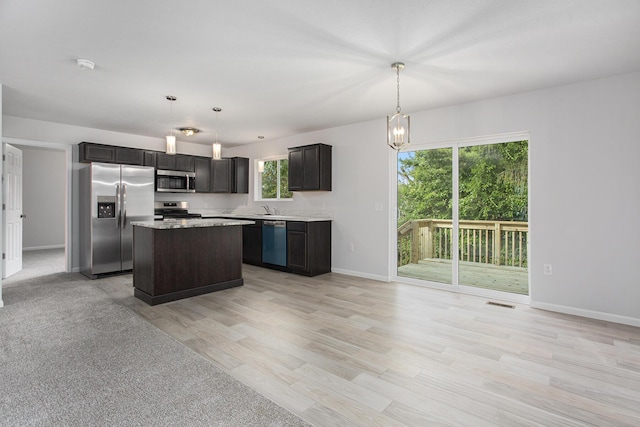 kitchen with stainless steel appliances, a kitchen island, hanging light fixtures, and light hardwood / wood-style flooring