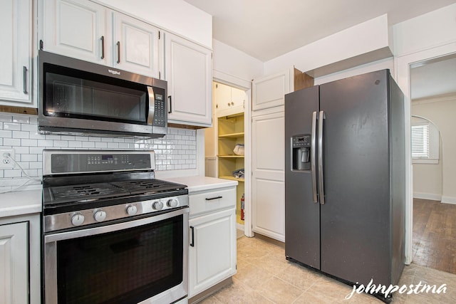 kitchen with backsplash, light tile patterned flooring, white cabinets, and appliances with stainless steel finishes