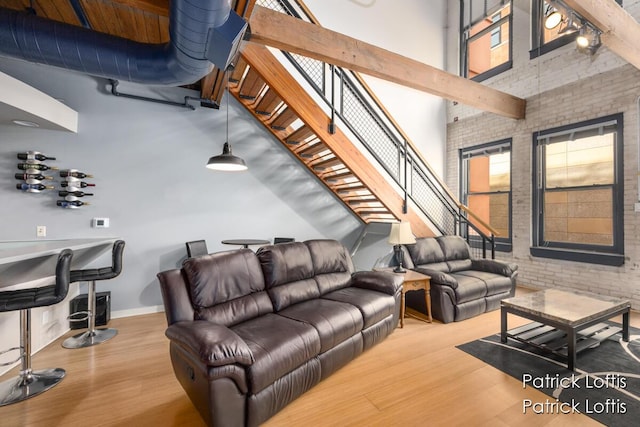 living room featuring a towering ceiling, wood-type flooring, and brick wall