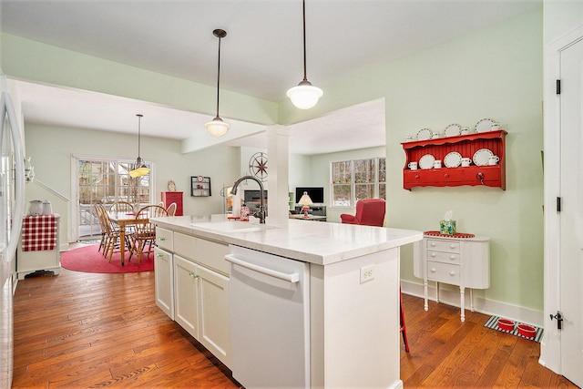 kitchen featuring pendant lighting, sink, white dishwasher, and an island with sink