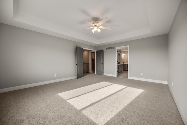 unfurnished bedroom with ensuite bathroom, carpet flooring, ceiling fan, and a tray ceiling