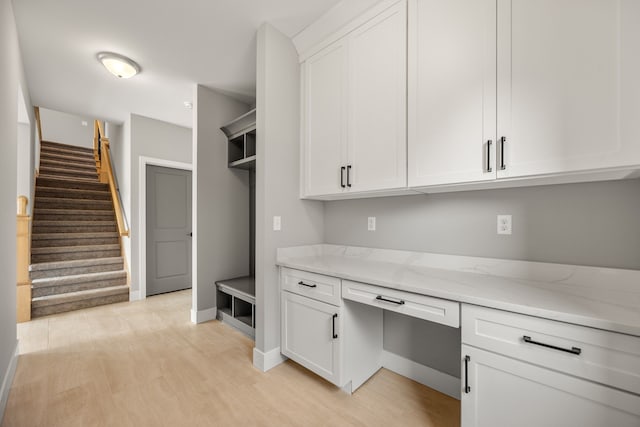 interior space featuring white cabinetry, light wood-type flooring, built in desk, and light stone counters