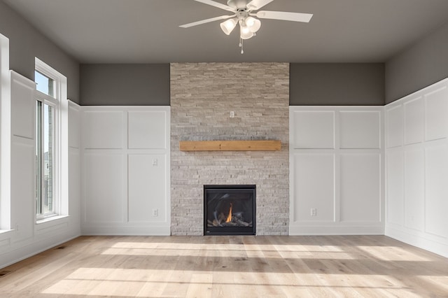 unfurnished living room featuring ceiling fan, a stone fireplace, and light hardwood / wood-style flooring