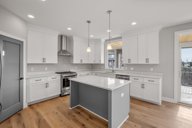 kitchen featuring white cabinetry, a center island, hanging light fixtures, appliances with stainless steel finishes, and wall chimney range hood