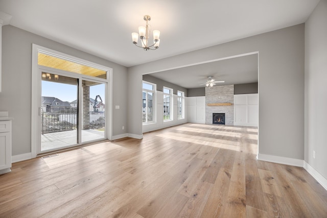 unfurnished living room featuring a stone fireplace, ceiling fan with notable chandelier, and light hardwood / wood-style flooring