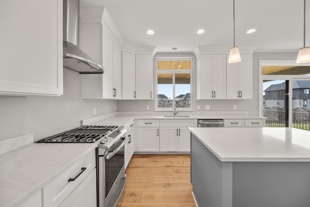 kitchen featuring stainless steel appliances, light hardwood / wood-style floors, white cabinets, decorative light fixtures, and wall chimney exhaust hood