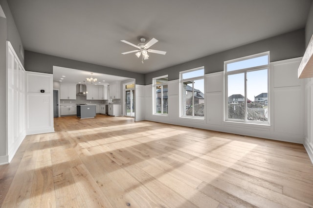 unfurnished living room featuring ceiling fan with notable chandelier and light wood-type flooring