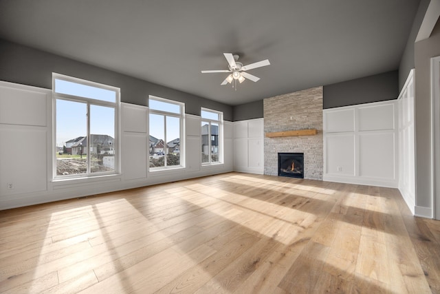 unfurnished living room featuring a stone fireplace, ceiling fan, and light hardwood / wood-style flooring