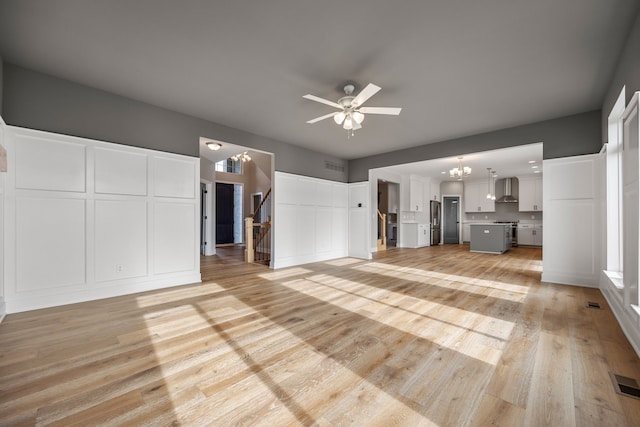 unfurnished living room with ceiling fan with notable chandelier and light hardwood / wood-style flooring