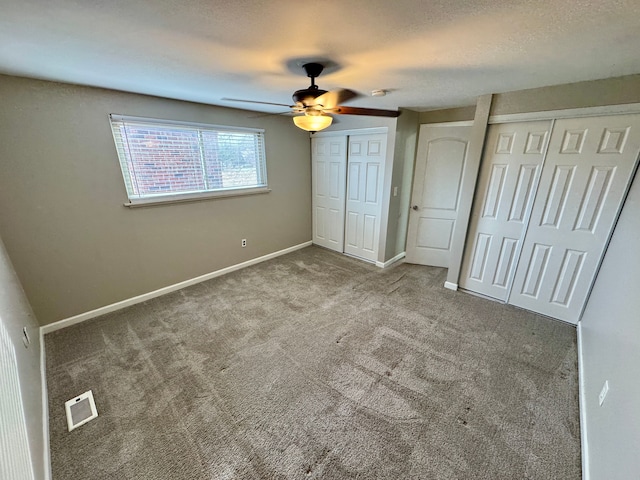 unfurnished bedroom featuring ceiling fan, two closets, light colored carpet, and a textured ceiling