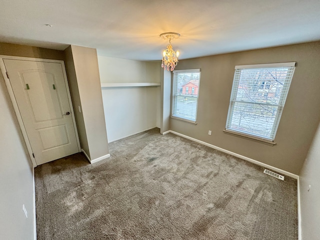 carpeted spare room featuring an inviting chandelier