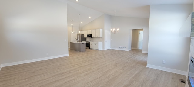 unfurnished living room with high vaulted ceiling, an inviting chandelier, and light hardwood / wood-style floors