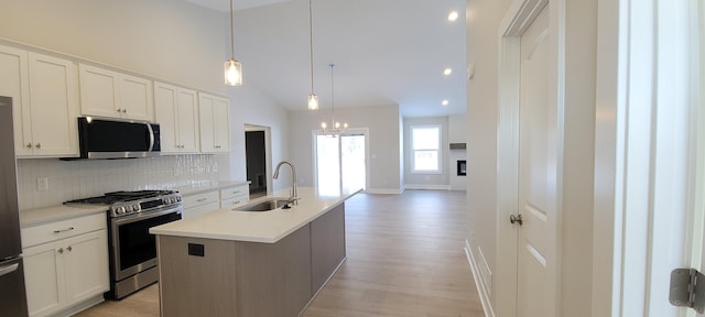 kitchen with decorative light fixtures, an island with sink, sink, white cabinets, and stainless steel appliances