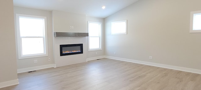 unfurnished living room featuring plenty of natural light, vaulted ceiling, and light wood-type flooring