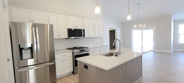 kitchen with appliances with stainless steel finishes, decorative light fixtures, sink, white cabinets, and a kitchen island with sink