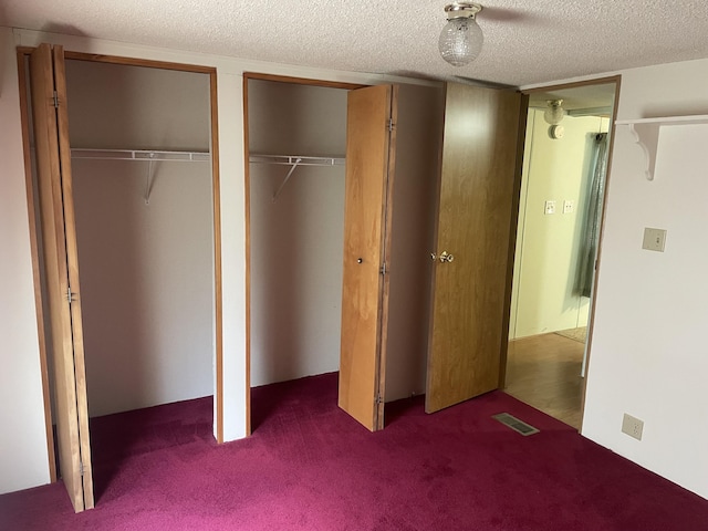 unfurnished bedroom featuring carpet, a textured ceiling, and two closets