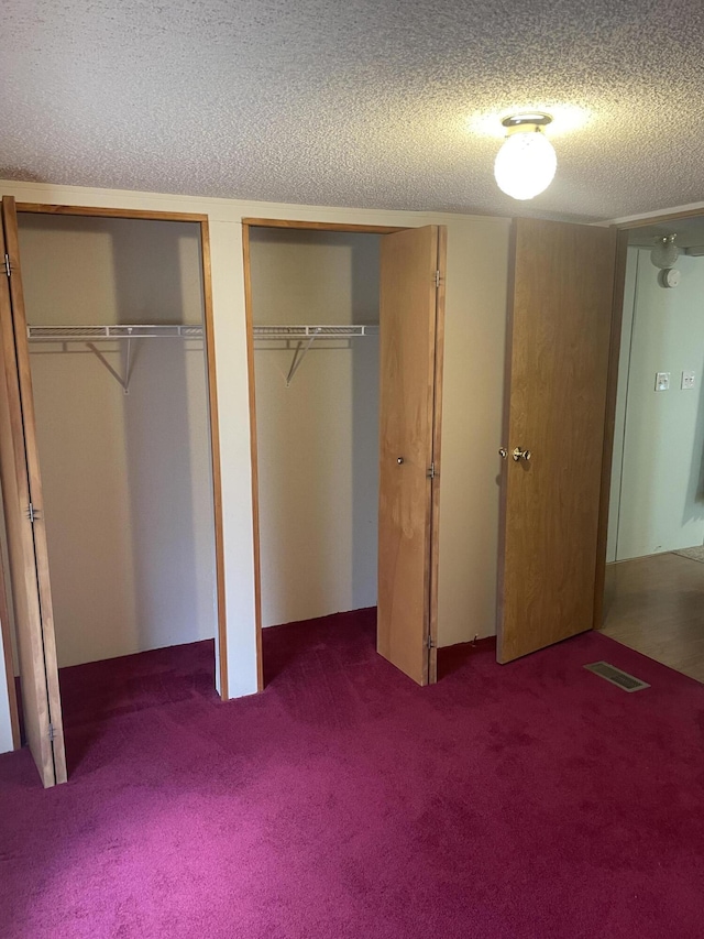 unfurnished bedroom featuring a textured ceiling, multiple closets, and dark colored carpet