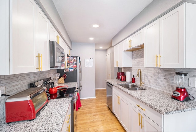 kitchen with sink, white cabinetry, stainless steel appliances, light stone countertops, and light wood-type flooring