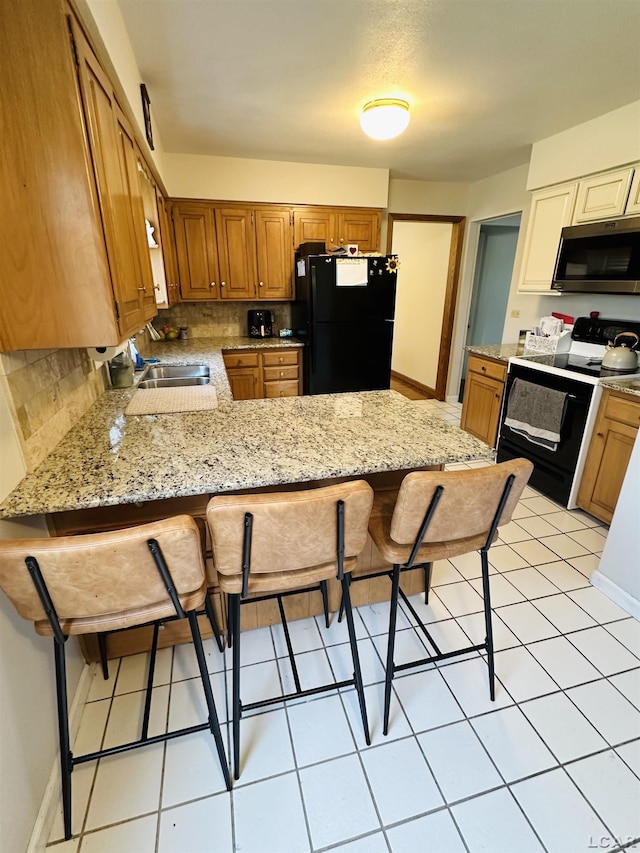 kitchen with electric stove, a kitchen breakfast bar, light stone counters, black fridge, and kitchen peninsula