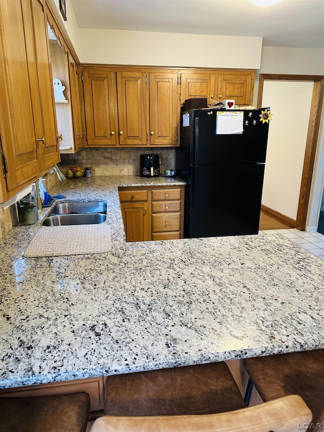 kitchen featuring black fridge, decorative backsplash, a breakfast bar, and kitchen peninsula