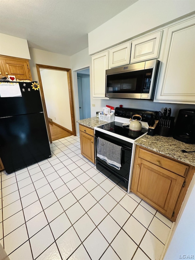 kitchen with black fridge, light stone counters, electric range, and cream cabinets