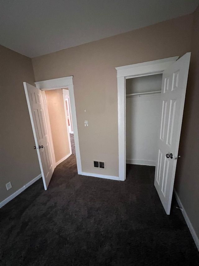 unfurnished bedroom with a closet and dark colored carpet