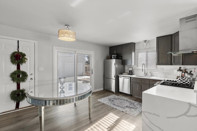 kitchen featuring sink, wall chimney range hood, light hardwood / wood-style flooring, stainless steel appliances, and light stone countertops