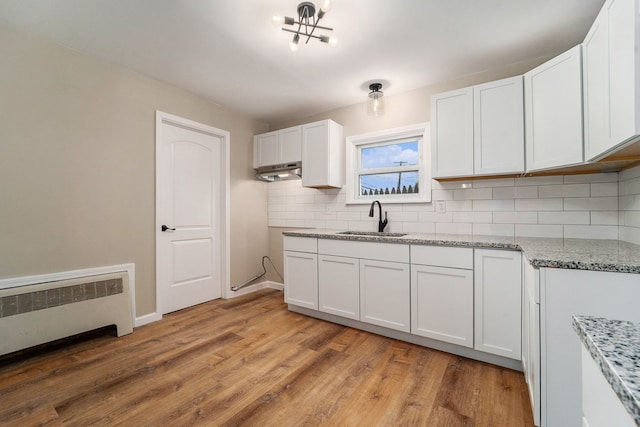 kitchen featuring sink, radiator heating unit, white cabinets, light hardwood / wood-style floors, and backsplash