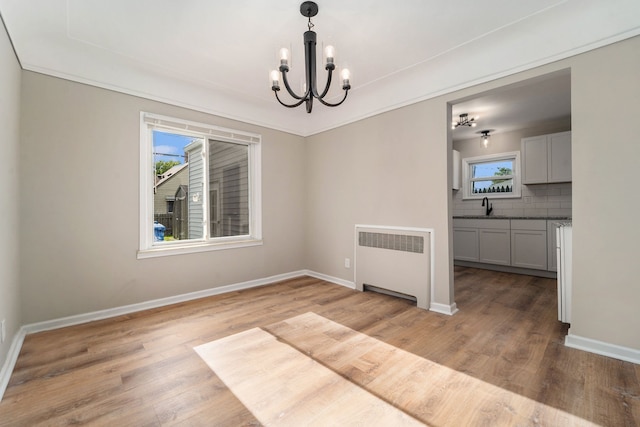 unfurnished dining area with radiator, sink, light hardwood / wood-style flooring, and a notable chandelier