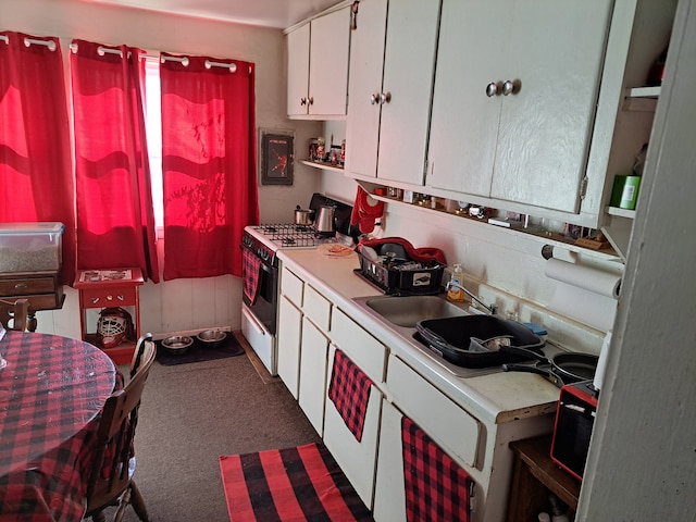 kitchen featuring white cabinetry, sink, white gas range oven, and dark colored carpet